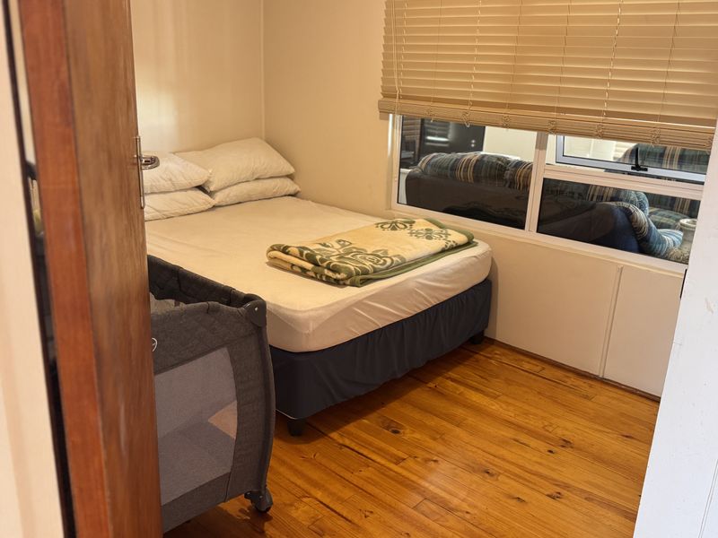 A compact bedroom featuring polished timber flooring and a large window fitted with venetian blinds, providing natural light.