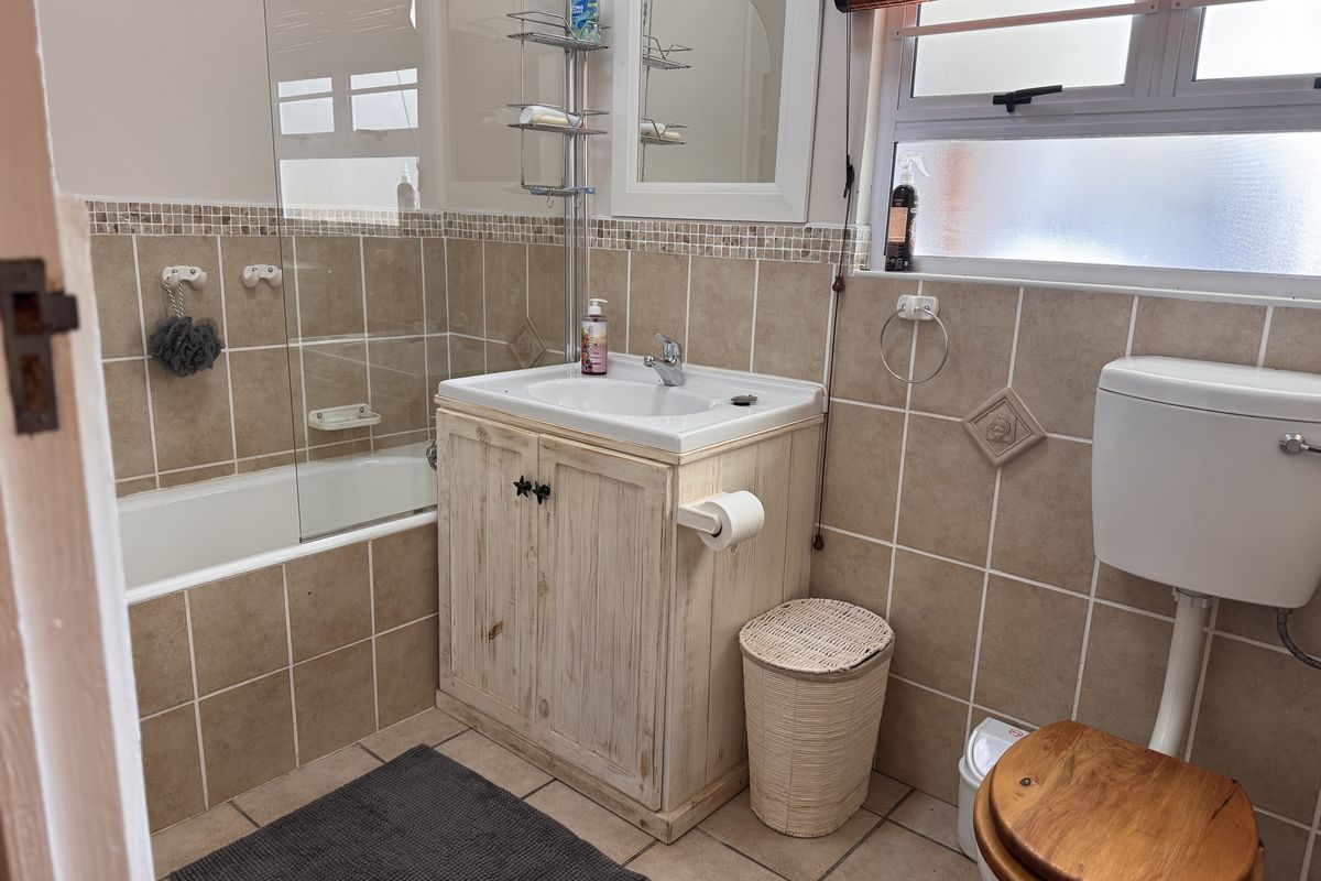 A functional bathroom featuring a bathtub with a glass screen, a vanity cabinet with a basin, and a toilet, finished with neutral wall tiles.