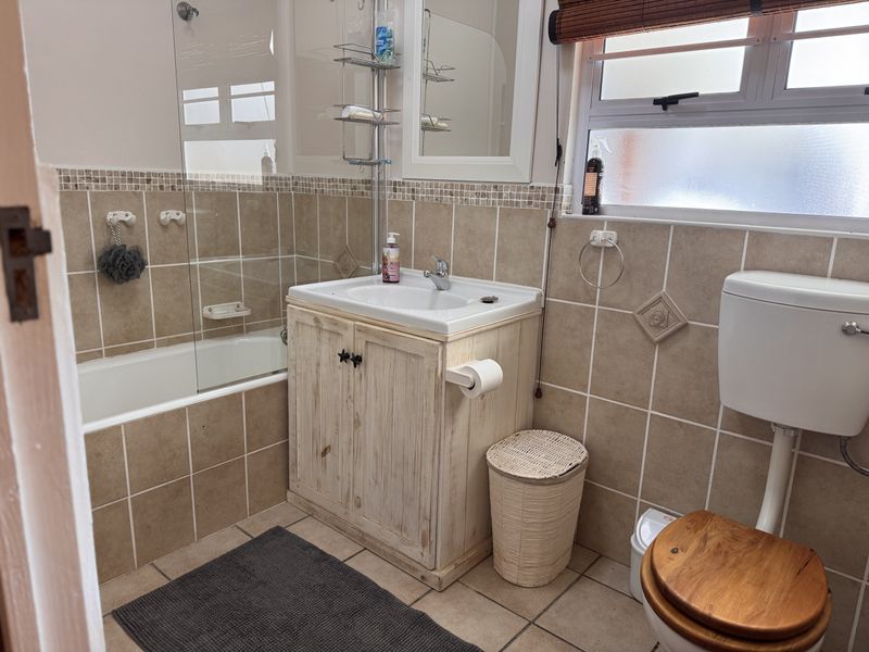 A functional bathroom featuring a bathtub with a glass screen, a vanity cabinet with a basin, and a toilet, finished with neutral wall tiles.