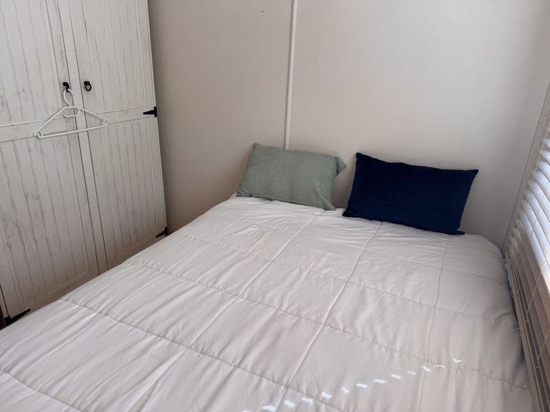 A compact bedroom featuring a built-in wardrobe and venetian blinds, providing a functional and neutral space.