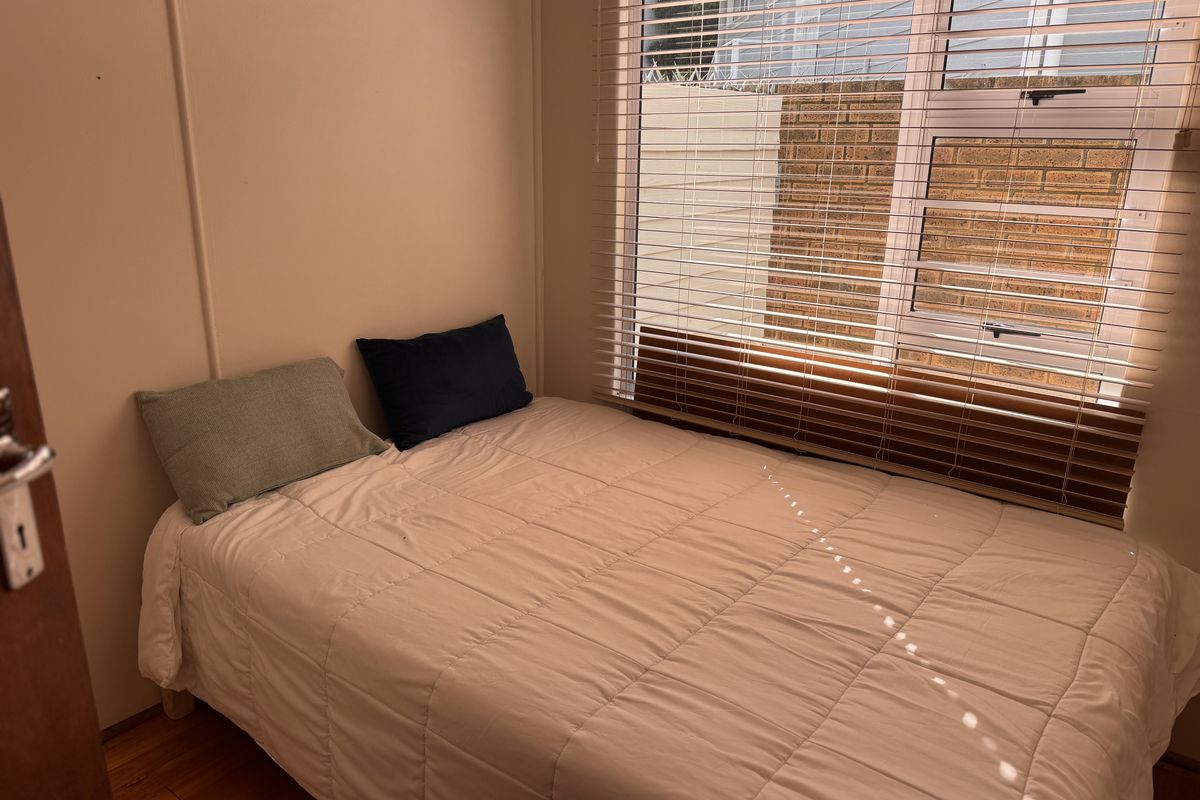 A compact bedroom featuring timber flooring and venetian blinds, providing a functional space with natural light.