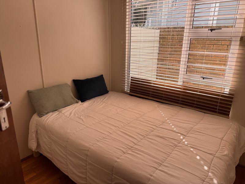 A compact bedroom featuring timber flooring and venetian blinds, providing a functional space with natural light.