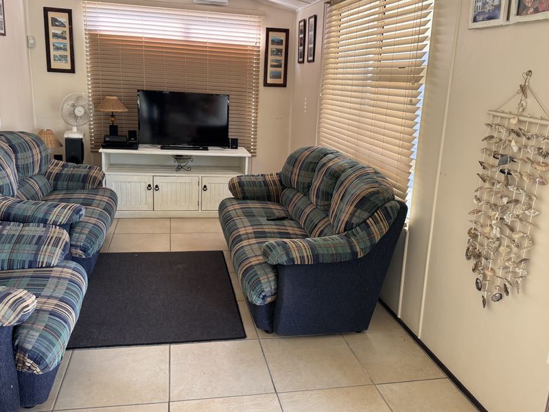 A comfortable living room featuring tiled flooring and large windows with venetian blinds, providing a functional and well-lit space.