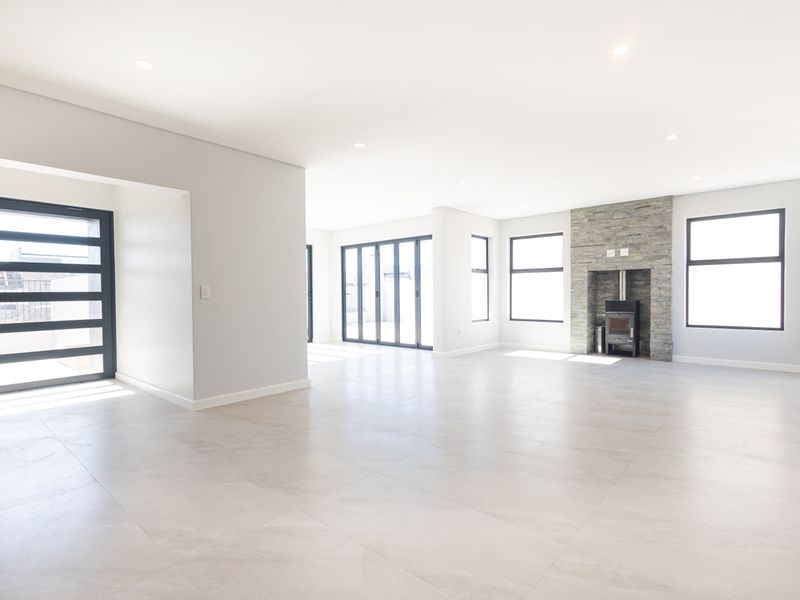 Spacious open-plan living area featuring large format floor tiles, a striking stone-clad fireplace with a wood-burning stove, and expansive aluminium-framed doors and windows.