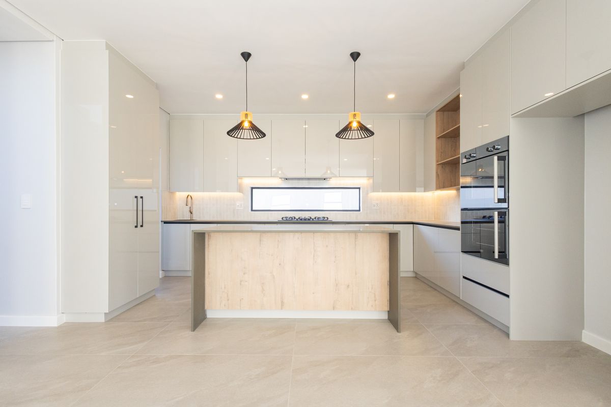 Modern, high-end kitchen featuring sleek cabinetry, a central island, built-in appliances, and contemporary lighting, finished with neutral tiled flooring.