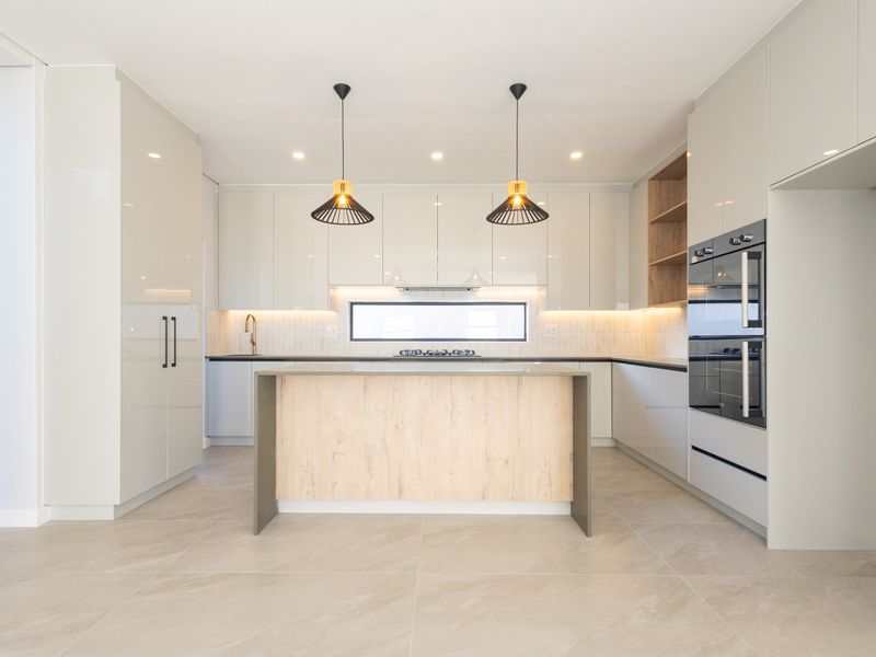 Modern, high-end kitchen featuring sleek cabinetry, a central island, built-in appliances, and contemporary lighting, finished with neutral tiled flooring.