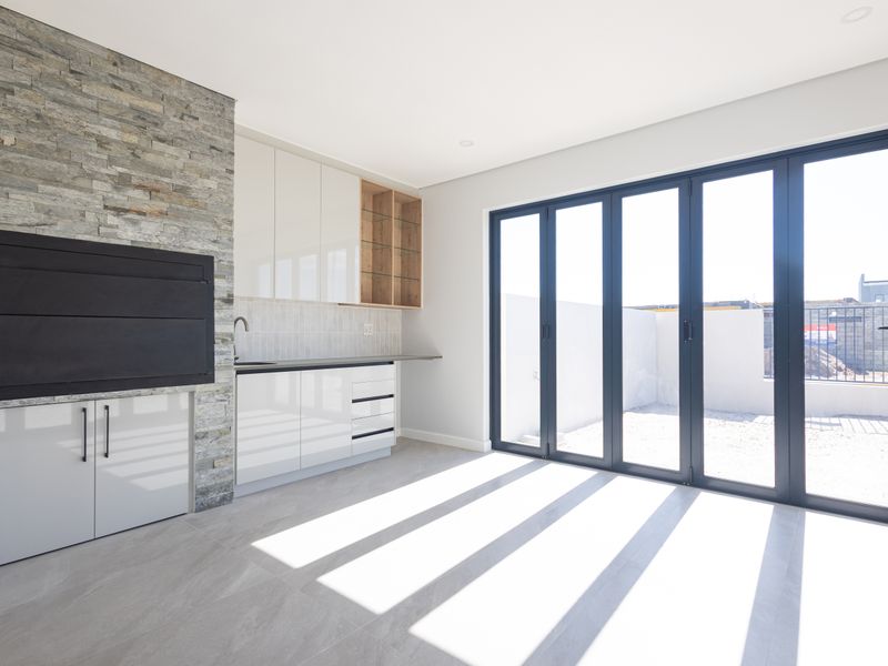 Modern living area featuring a built-in braai with stone cladding, kitchenette cabinetry, and large bi-fold doors opening to an outdoor space.