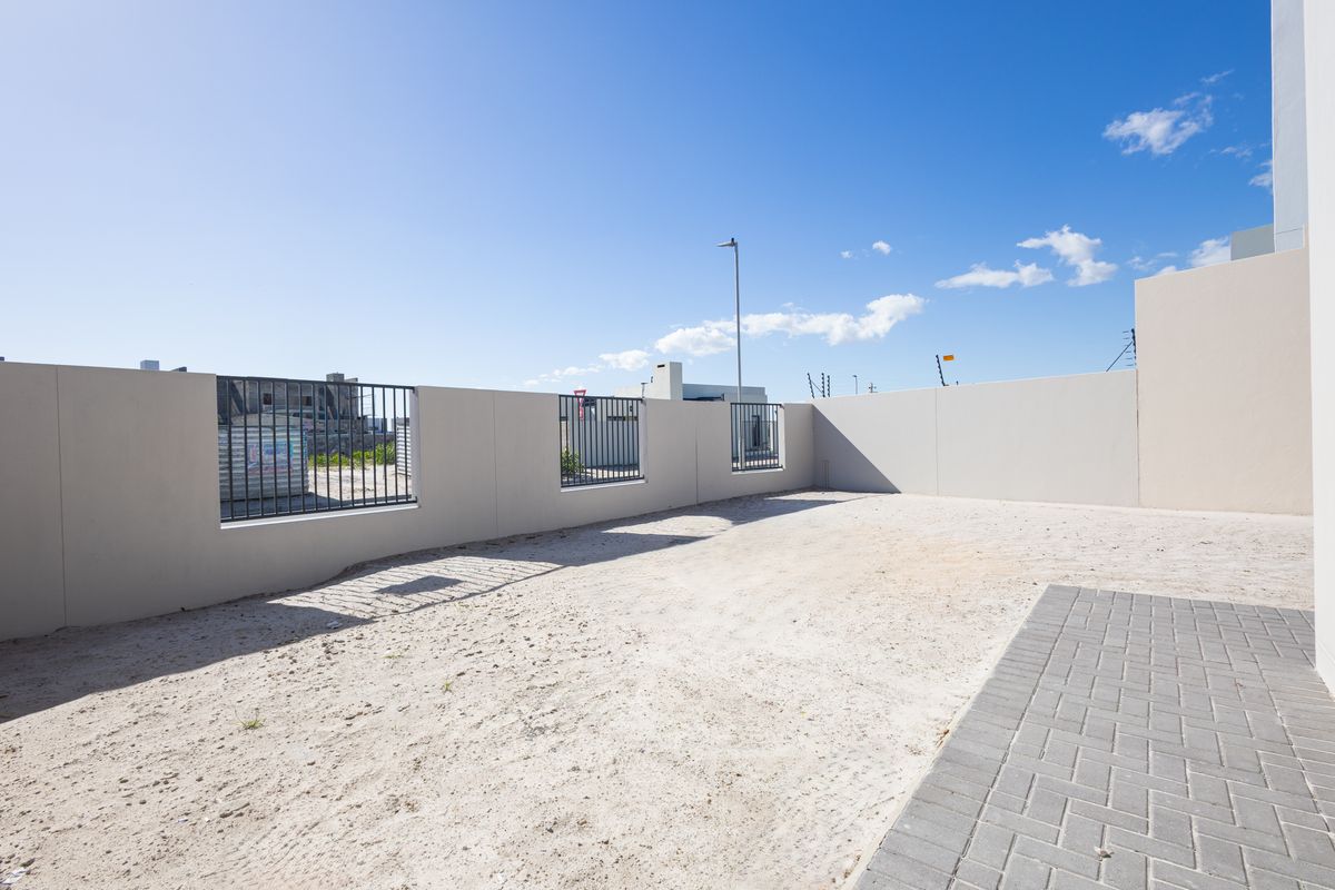 A spacious, undeveloped rear yard featuring a paved walkway, perimeter boundary walls with metal fencing, and an open area ready for landscaping.