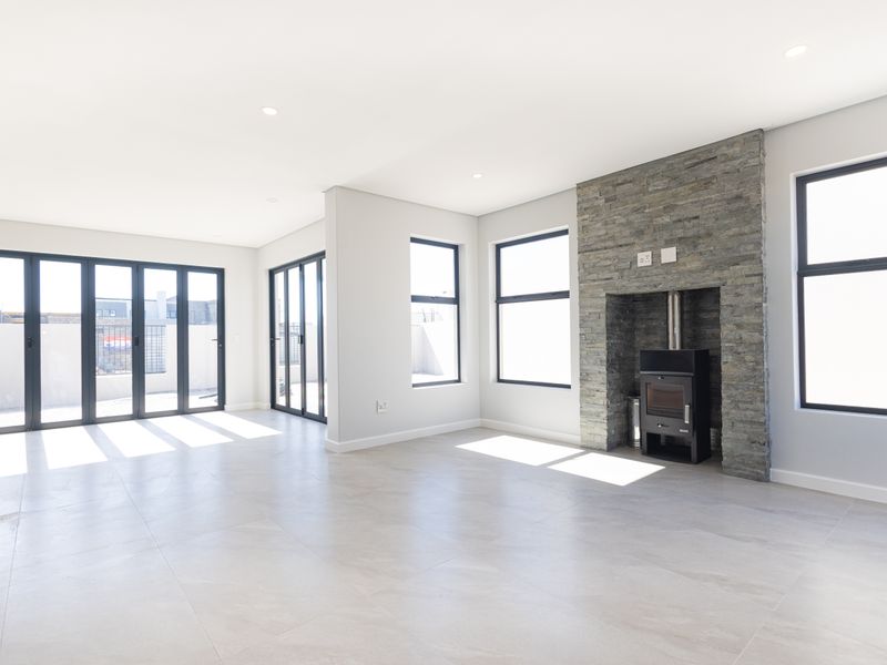 Spacious, light-filled living area featuring a striking stone-clad fireplace with a wood-burning stove, large windows, and modern aluminium stacker doors leading outdoors.