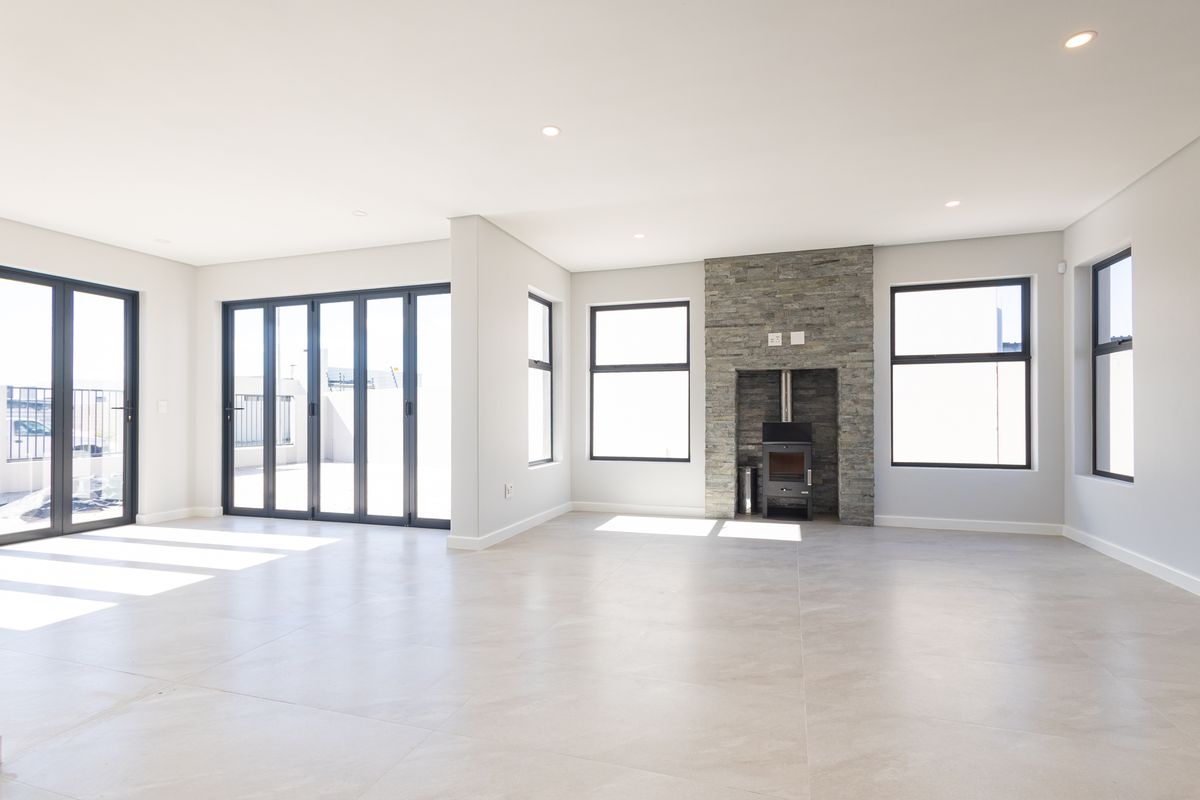 Spacious, light-filled living area featuring modern tiled flooring, a striking stone-clad fireplace with a wood-burning stove, and large sliding doors leading to the patio.