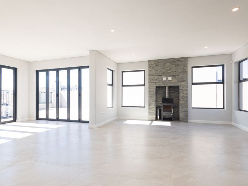 Spacious, light-filled living area featuring modern tiled flooring, a striking stone-clad fireplace with a wood-burning stove, and large sliding doors leading to the patio.