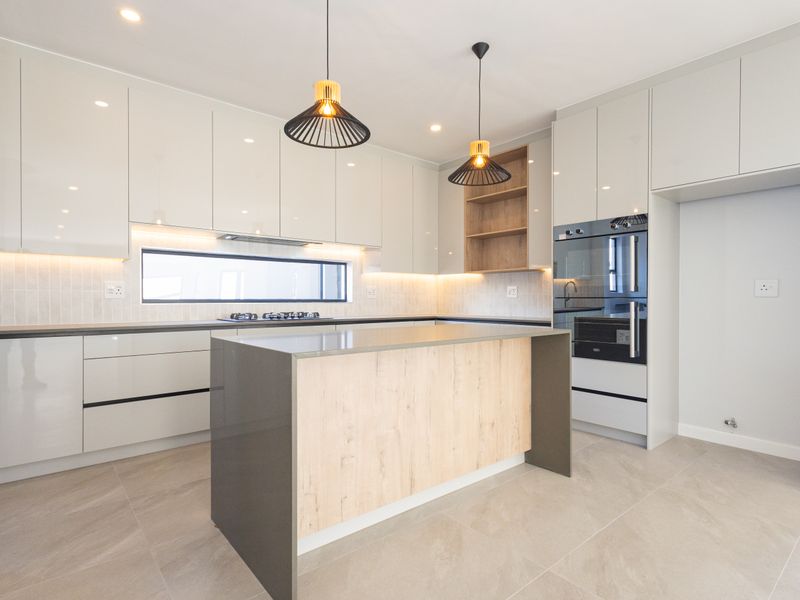 Modern kitchen featuring sleek high-gloss cabinetry, a central island with stone countertop, integrated oven, gas hob, and stylish pendant lighting.
