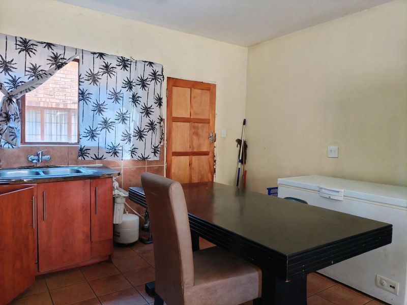 A functional kitchen area featuring wooden cabinetry, a stainless steel sink, tiled backsplash, and tiled flooring, with a wooden door leading to another room.