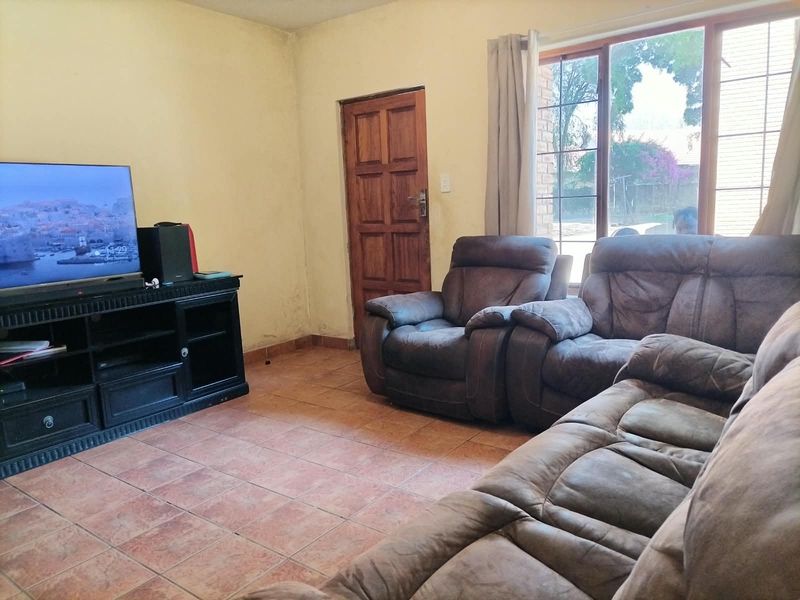 A living room featuring tiled flooring, a timber door, and a large window, currently showing signs of wear on the walls.