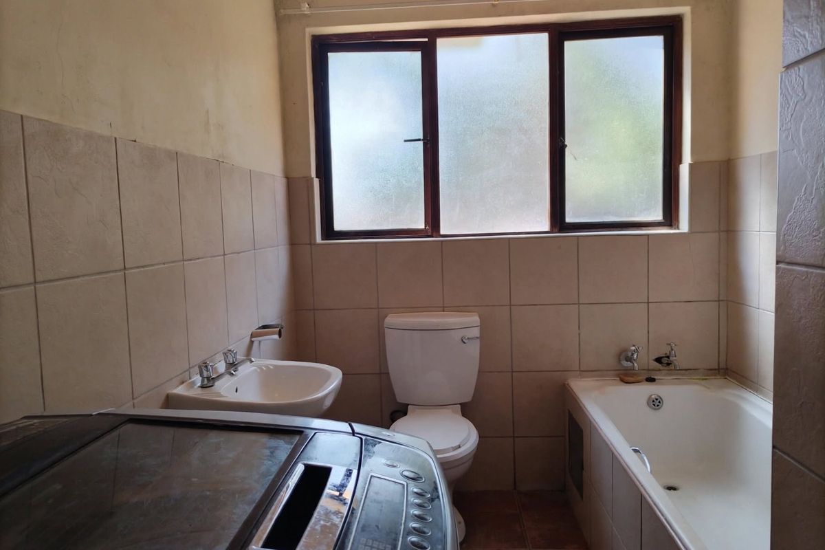 A functional bathroom featuring a bathtub, toilet, and washbasin with neutral wall and floor tiling, requiring cosmetic updates to improve its overall condition.