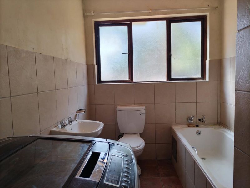A functional bathroom featuring a bathtub, toilet, and washbasin with neutral wall and floor tiling, requiring cosmetic updates to improve its overall condition.