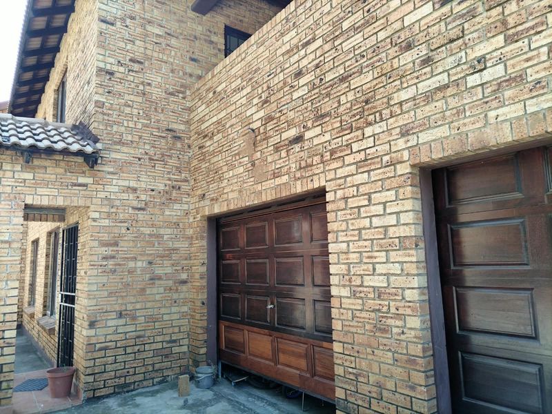 Exterior view of the apartment building featuring a face brick facade, wooden garage doors, and a tiled roof structure.