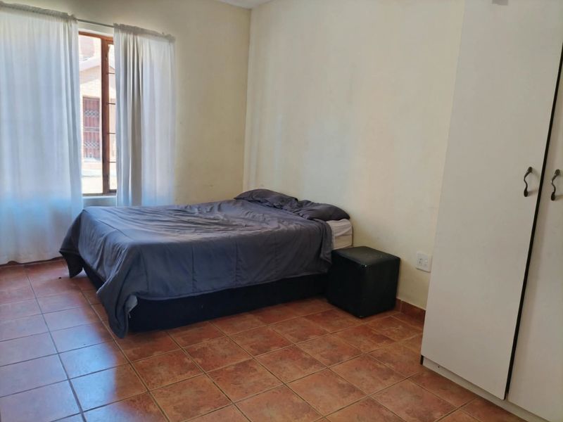 A functional bedroom featuring tiled flooring, a built-in wardrobe, and natural light from a window.