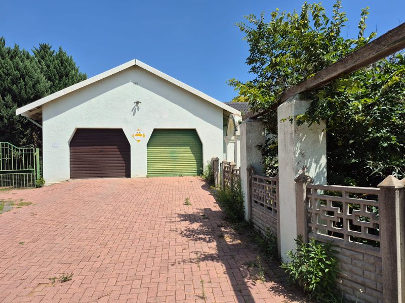 Front view of the property featuring a double garage with roll-up doors, a paved driveway, and a decorative boundary wall.