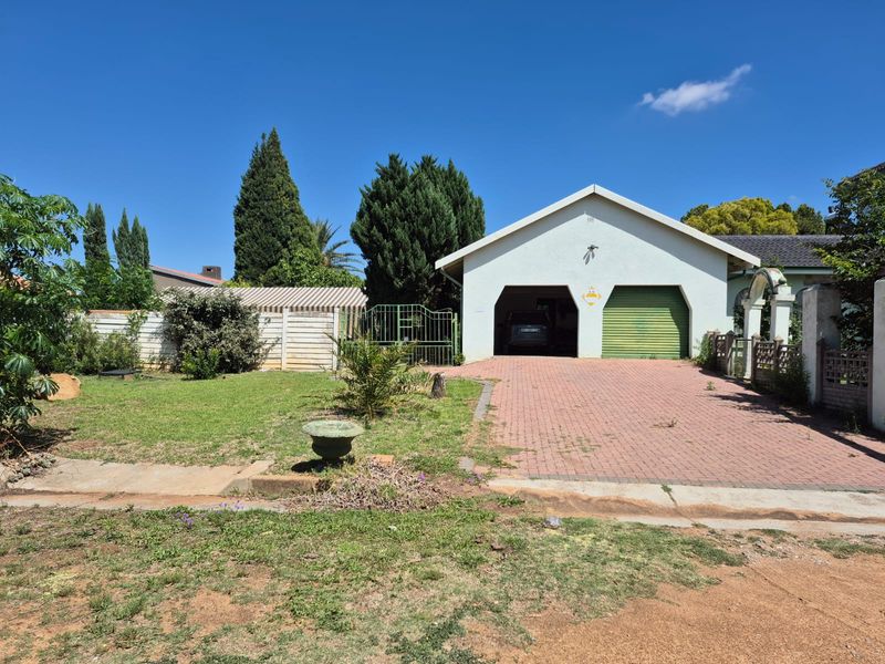 Front view of the property featuring a paved driveway, a double garage with one roll-up door, and a front garden area.