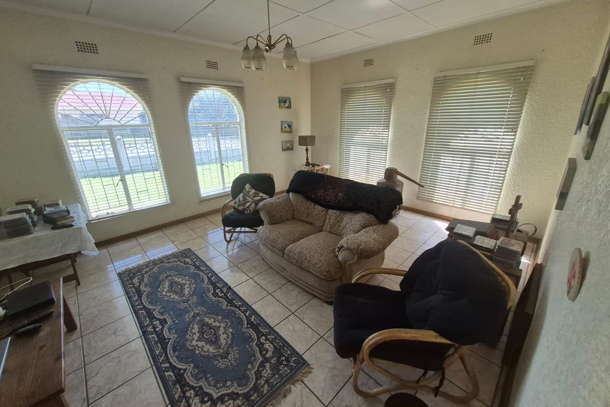 A living room featuring tiled flooring, arched windows with venetian blinds, and a classic pendant light fixture, offering a bright and functional living space.