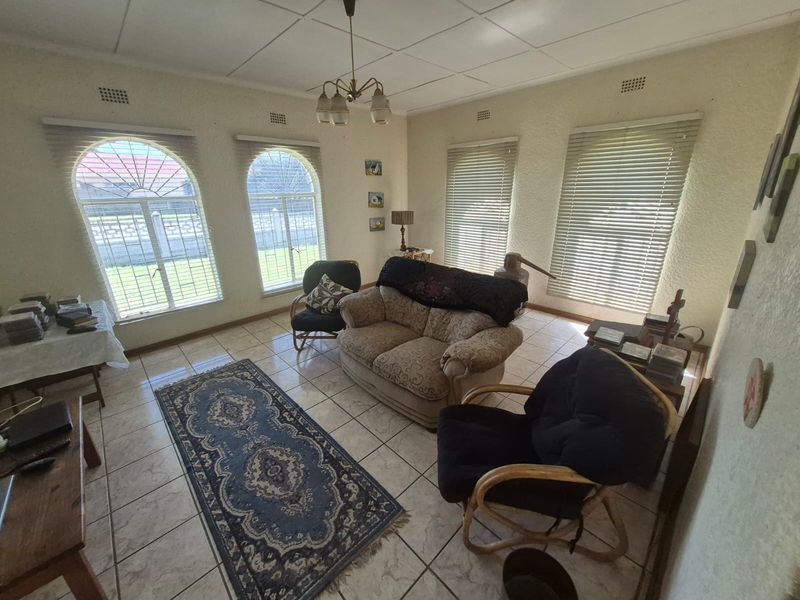 A living room featuring tiled flooring, arched windows with venetian blinds, and a classic pendant light fixture, offering a bright and functional living space.