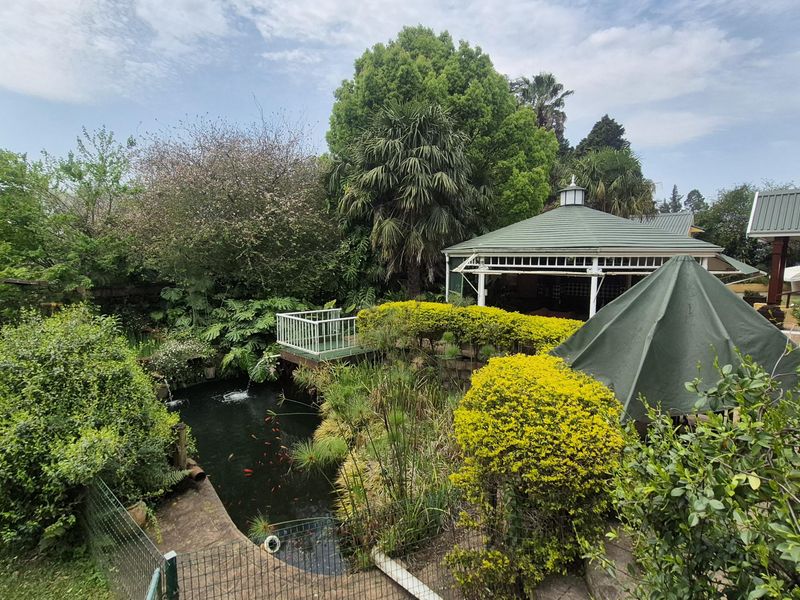 A lush, landscaped garden featuring a koi pond, a raised wooden deck, and a covered gazebo area, offering a tranquil outdoor retreat.