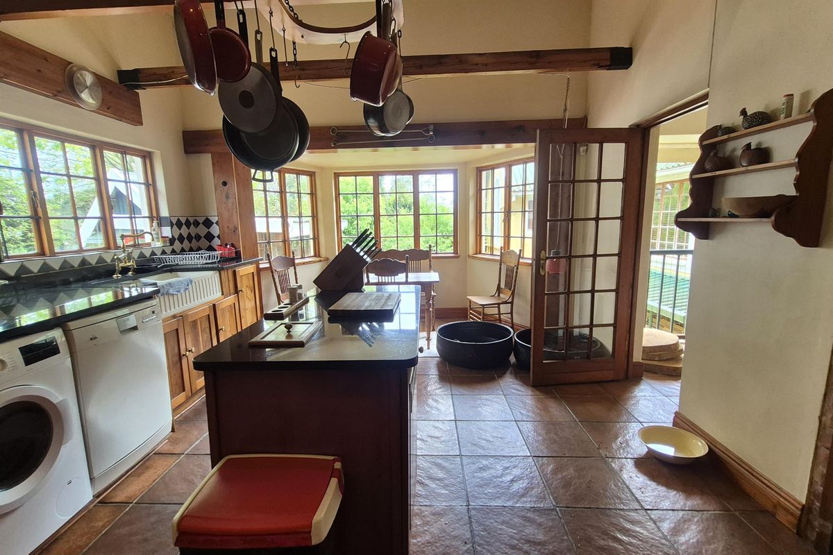 A rustic kitchen featuring timber cabinetry, granite countertops, a farmhouse sink, and exposed ceiling beams, with direct access to an outdoor area.