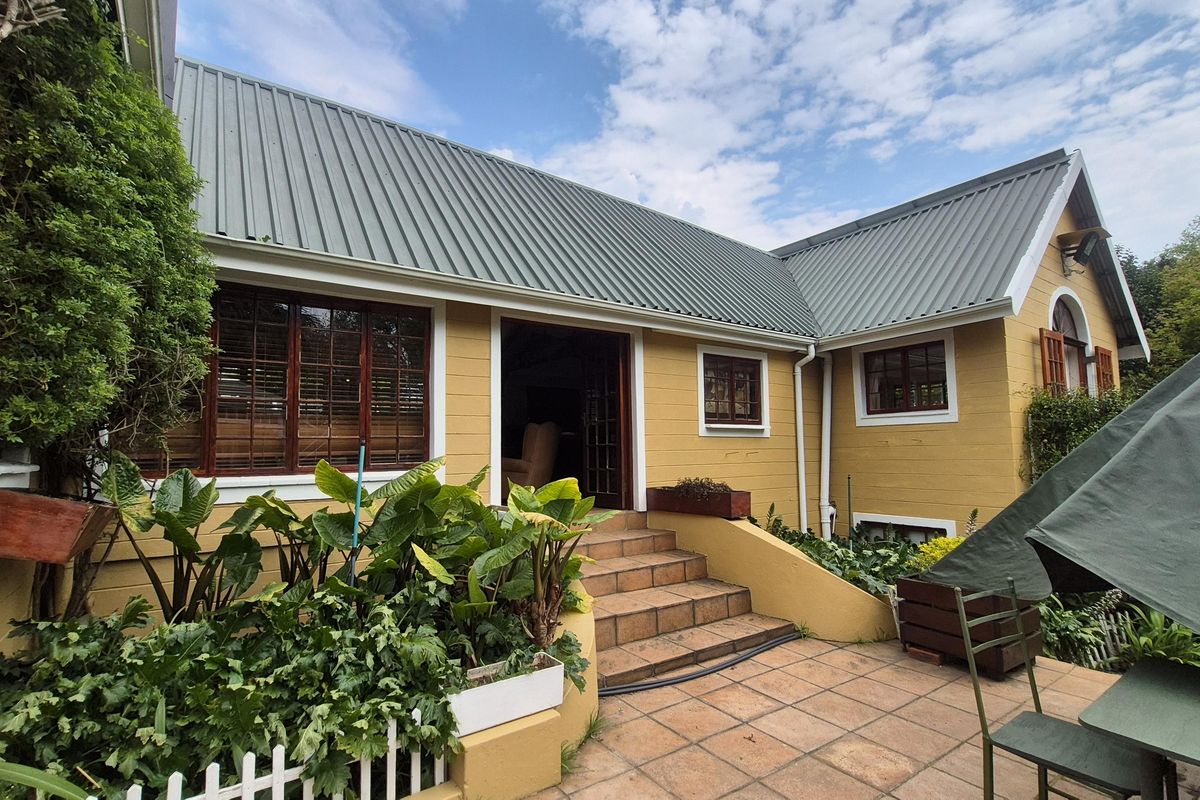 Rear exterior view of a house featuring yellow timber siding, a corrugated metal roof, and a tiled patio area with access steps.