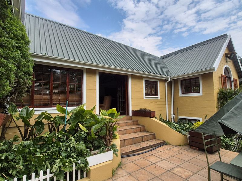 Rear exterior view of a house featuring yellow timber siding, a corrugated metal roof, and a tiled patio area with access steps.