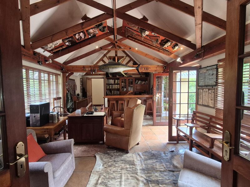 Spacious living area featuring vaulted ceilings with exposed timber trusses, tiled flooring, and a built-in wooden bar, offering a warm and rustic atmosphere.