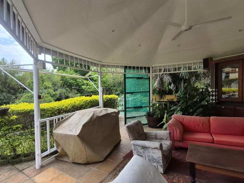A spacious covered patio featuring tiled flooring, a ceiling fan, recessed lighting, and built-in cabinetry, overlooking a lush garden area.