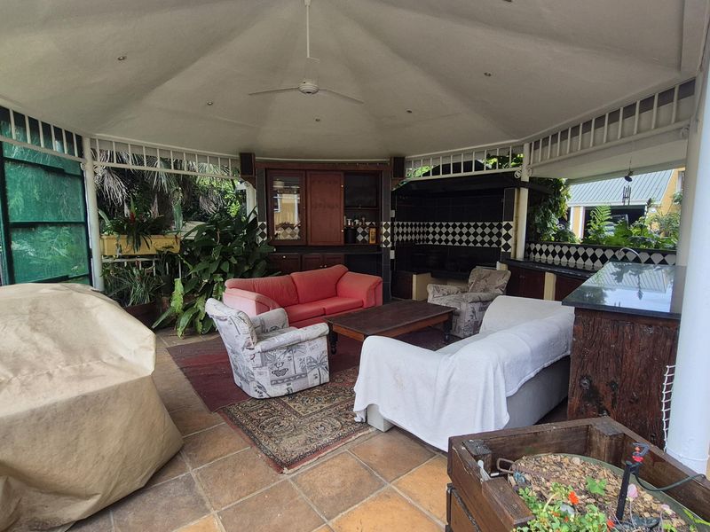 Covered outdoor patio area featuring a built-in braai, tiled flooring, ceiling fan, and integrated cabinetry with granite countertops.