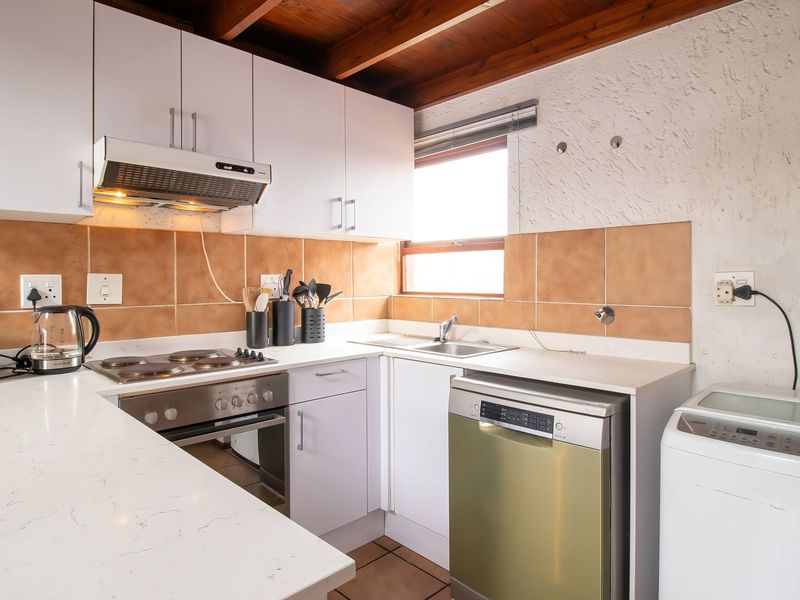 Compact kitchen featuring white cabinetry, tiled backsplash, built-in oven and hob, and exposed timber ceiling beams.