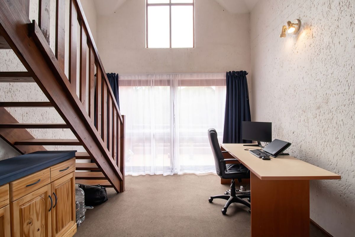 A bright living area featuring a wooden staircase, textured walls, and large windows providing natural light, with built-in cabinetry and carpeted flooring.