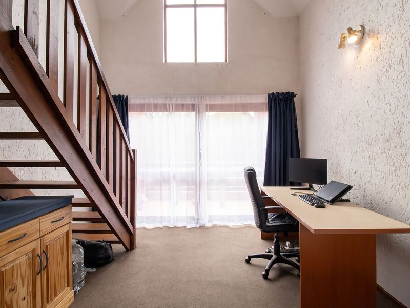A bright living area featuring a wooden staircase, textured walls, and large windows providing natural light, with built-in cabinetry and carpeted flooring.