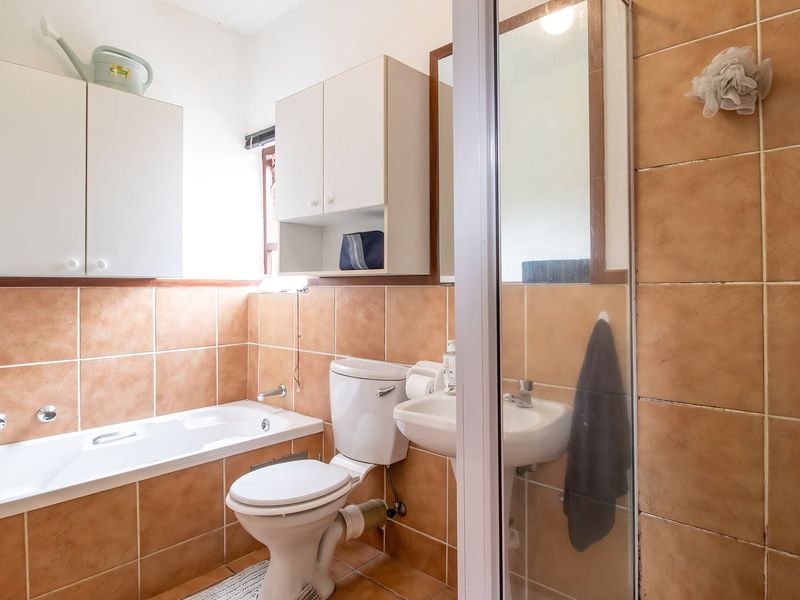 A functional bathroom featuring a bathtub, separate shower enclosure, pedestal sink, and built-in wall cabinetry with neutral ceramic tiling.