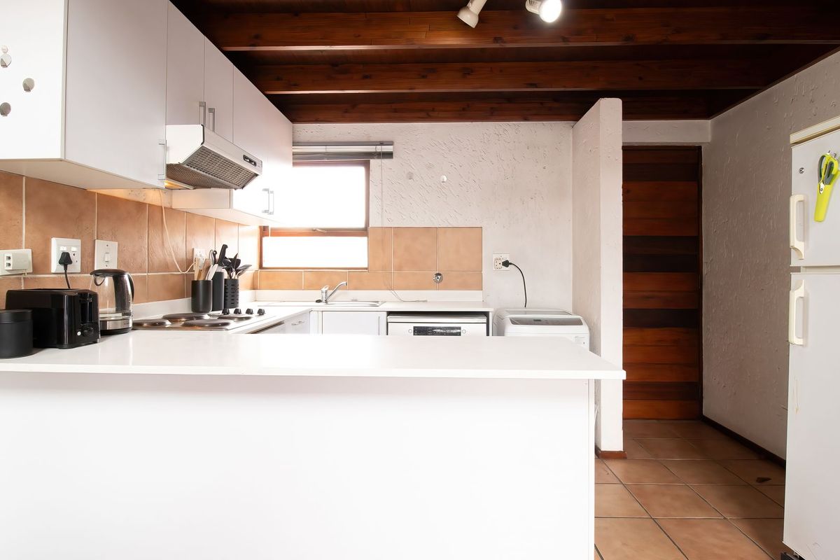 A functional kitchen featuring white cabinetry, a tiled backsplash, and exposed timber ceiling beams, offering a practical layout with integrated cooking and cleaning areas.