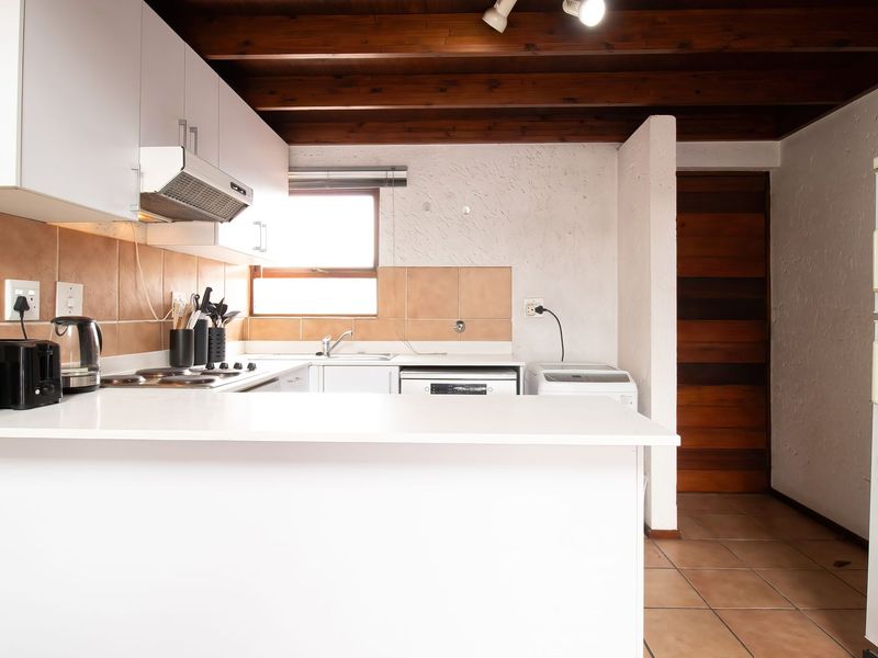 A functional kitchen featuring white cabinetry, a tiled backsplash, and exposed timber ceiling beams, offering a practical layout with integrated cooking and cleaning areas.