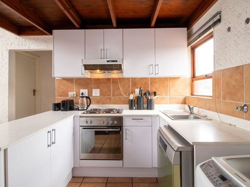 A functional kitchen featuring white cabinetry, built-in oven and hob, tiled backsplash, and exposed timber ceiling beams.