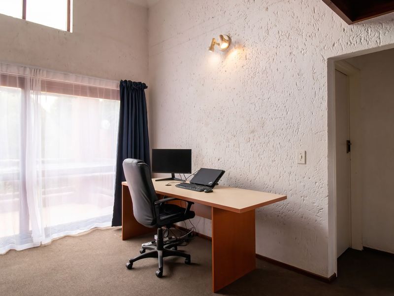 A functional office space featuring textured walls, carpet flooring, and a large sliding glass door providing natural light.