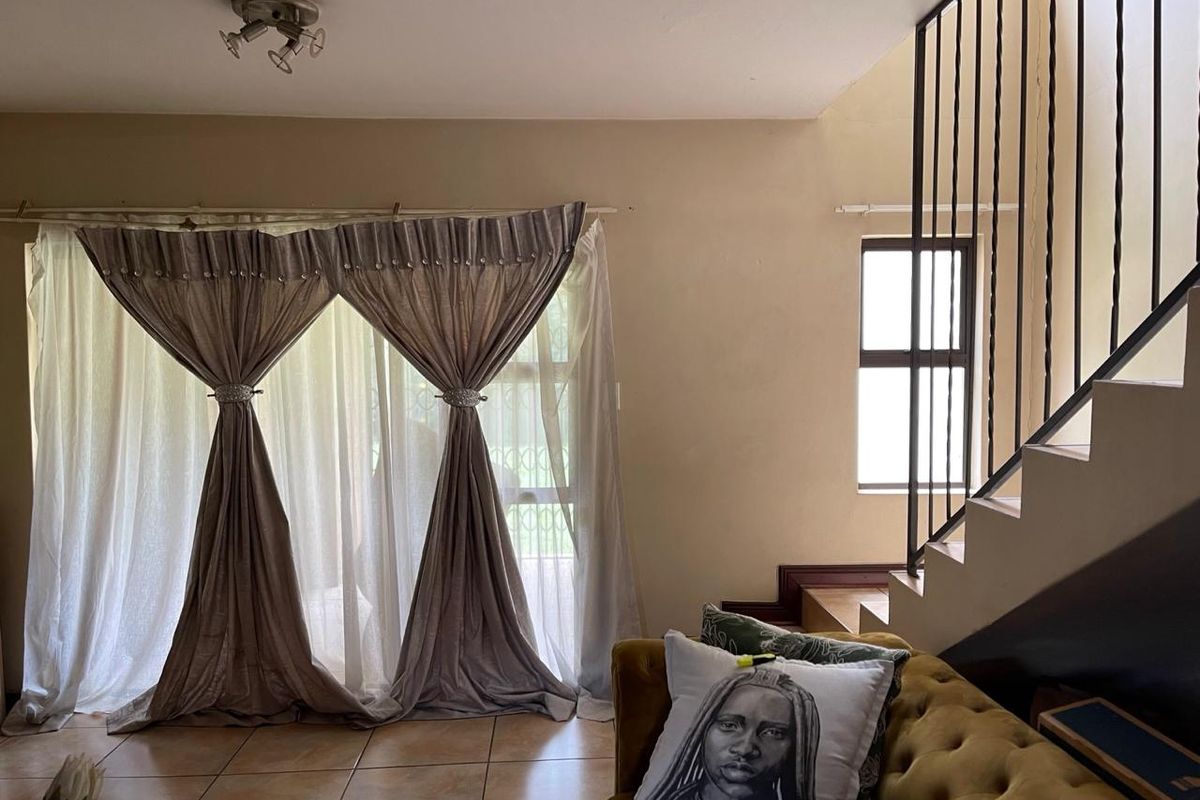 A living room area featuring tiled flooring, a staircase with a metal balustrade, and natural light from a window.