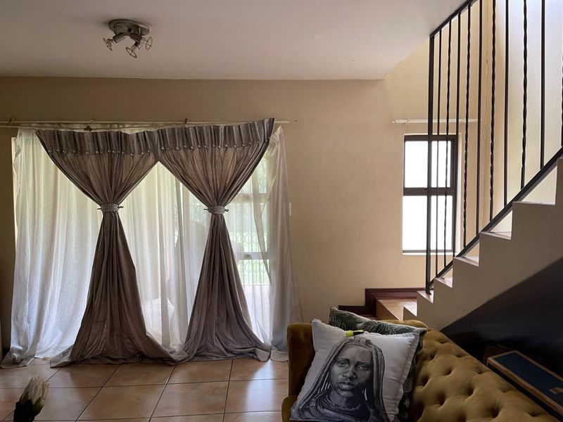 A living room area featuring tiled flooring, a staircase with a metal balustrade, and natural light from a window.