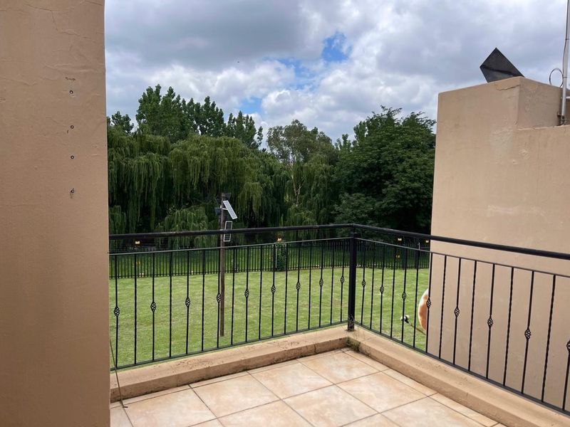A private balcony featuring tiled flooring and a wrought iron balustrade, offering a pleasant view of the surrounding garden and greenery.