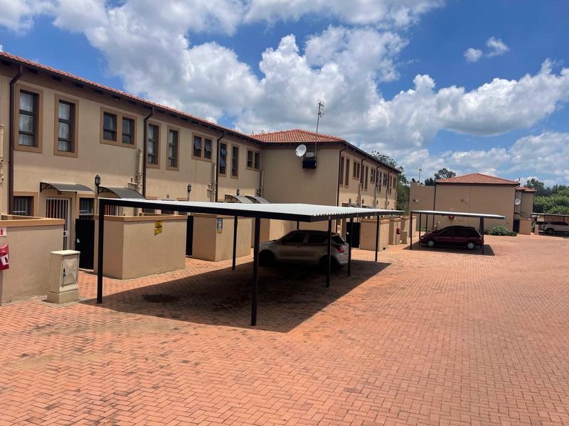 Exterior view of a townhouse complex featuring paved driveway areas and covered carports for resident parking.