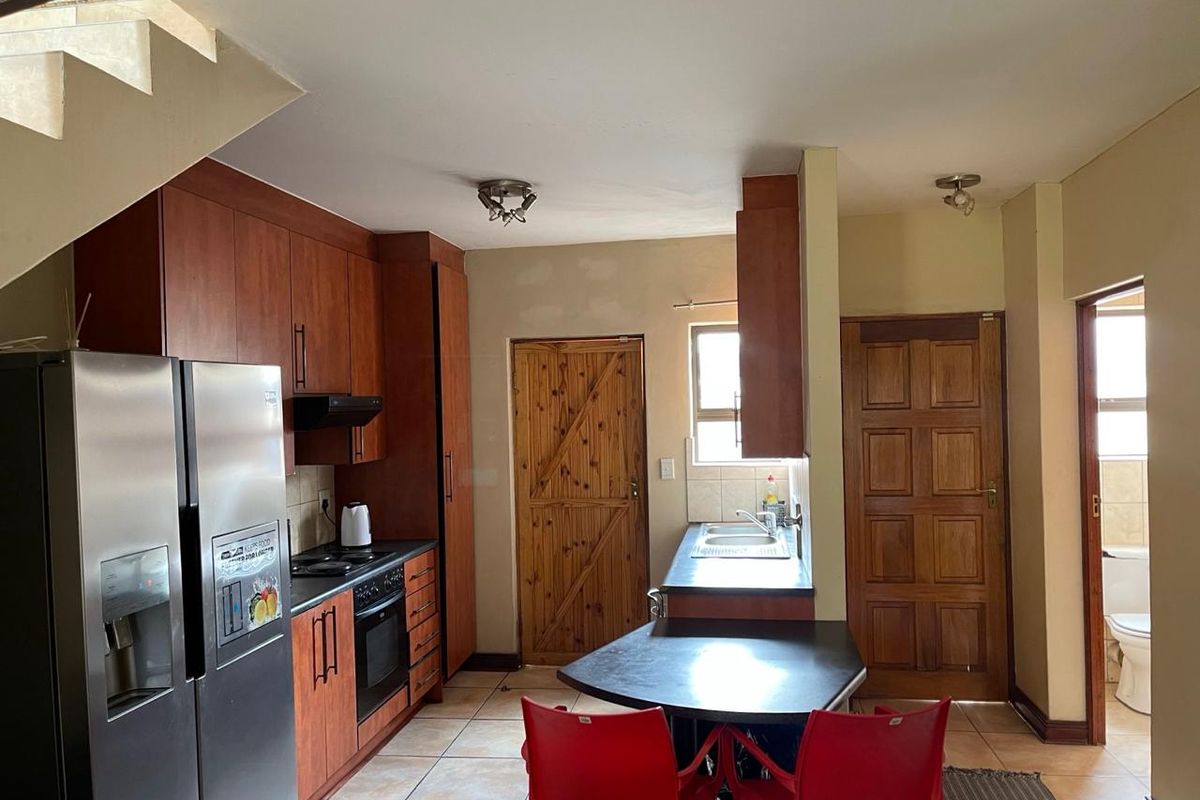 A functional kitchen featuring wood-finish cabinetry, laminate countertops, built-in oven, and tiled flooring, with an adjacent staircase and access to a bathroom.