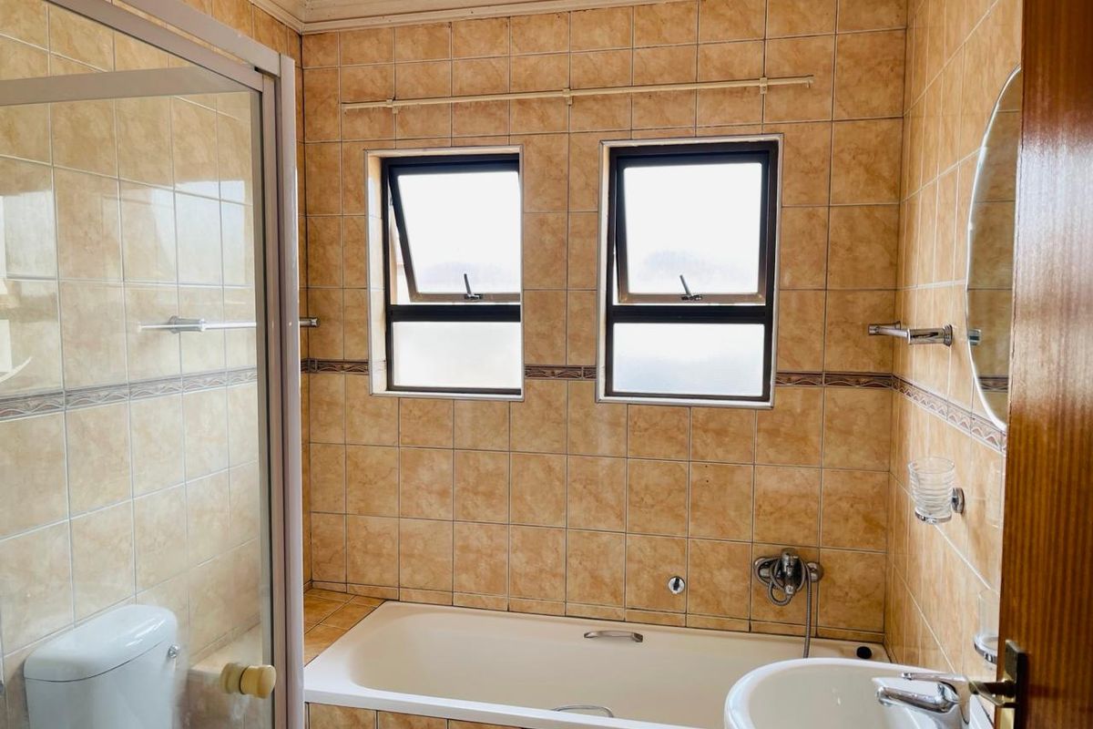 A functional bathroom featuring a built-in bathtub, separate shower enclosure, pedestal basin, and tiled finishes throughout.
