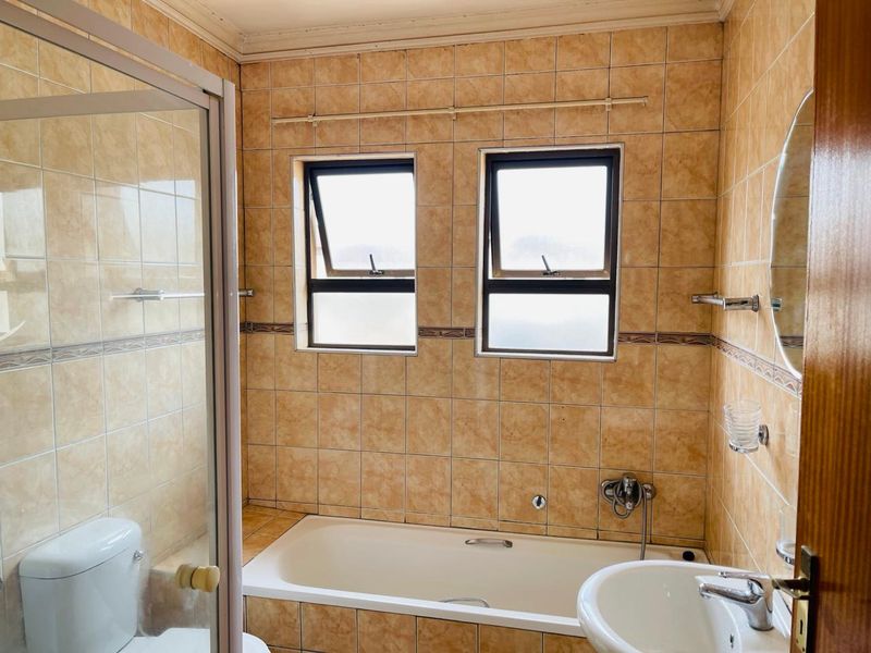 A functional bathroom featuring a built-in bathtub, separate shower enclosure, pedestal basin, and tiled finishes throughout.