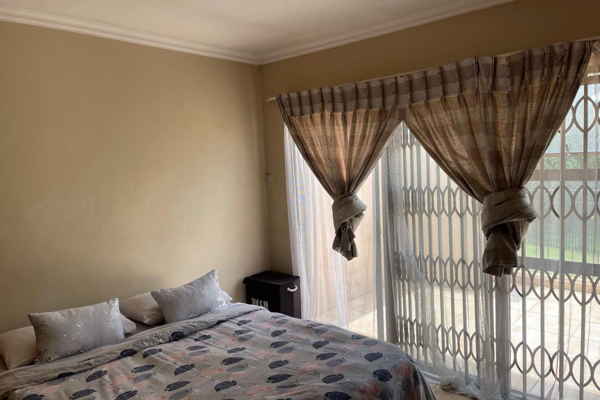 A bedroom featuring neutral wall tones, a sliding glass door with a security gate, and access to an outdoor area.