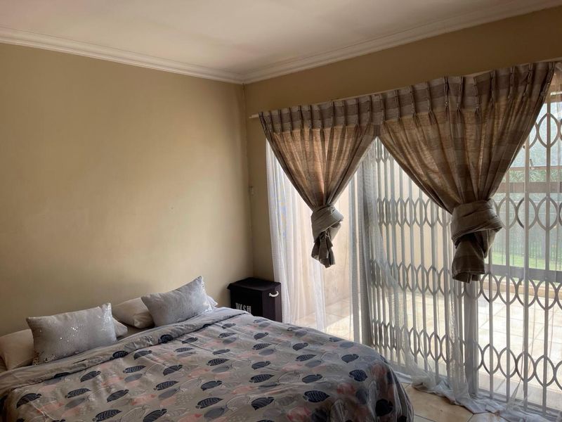 A bedroom featuring neutral wall tones, a sliding glass door with a security gate, and access to an outdoor area.